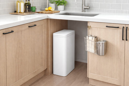 Slim white rectangular kitchen trash can placed neatly beside light wood cabinets under a modern sink in a small apartment kitchen, styled with clean countertops and minimal decor.